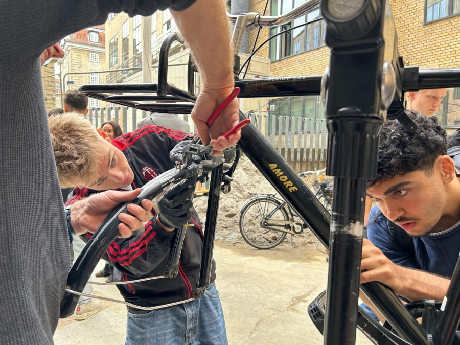 I gymnasiets gård er organisationen Medvind i fuld sving med at lære en gruppe elever at fikse cykler, der er blevet hængt op i medbragte kroge. Foto: Anne Burlund