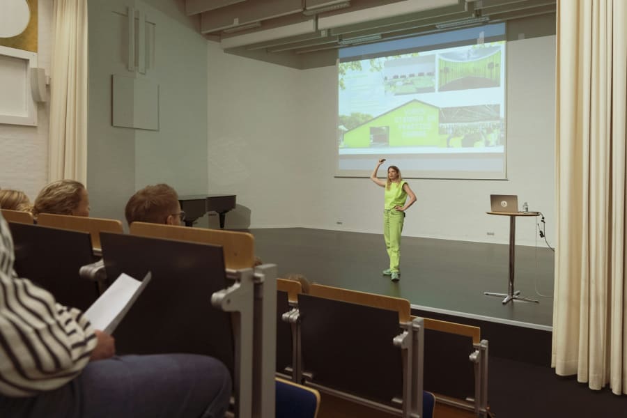 Julie Nymann holder foredrag iført den grønne farve, der er blevet et symbol i hendes kunstneriske praksis. Foto: Julie Nymann